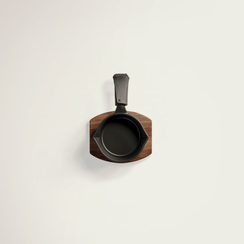 Small black cast iron skillet with wooden handle on a light gray background